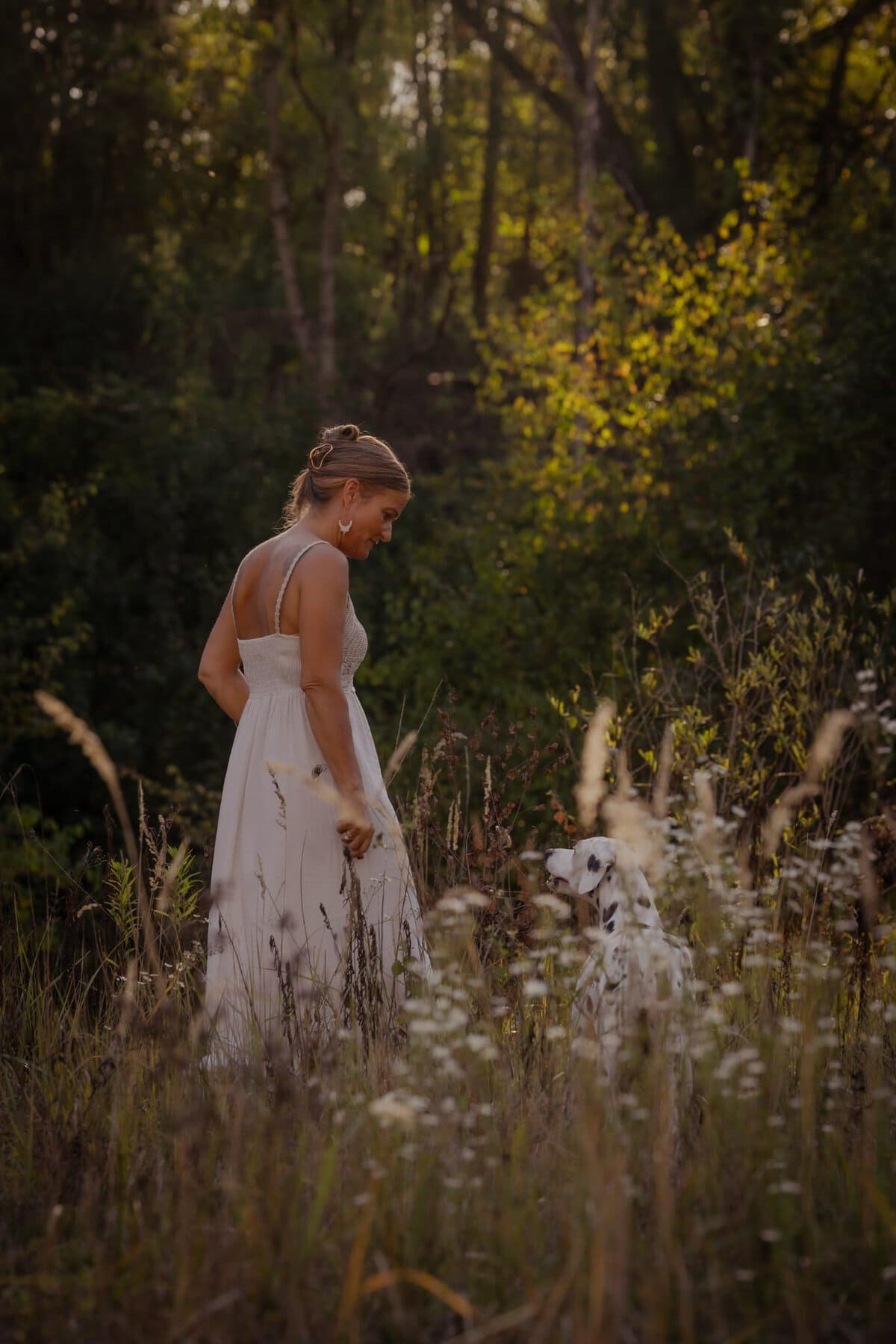 Karin steht im Abendlicht in einer Blumenwiese am Waldrand, ihr Dalmatiner Marla schaut zu ihr auf